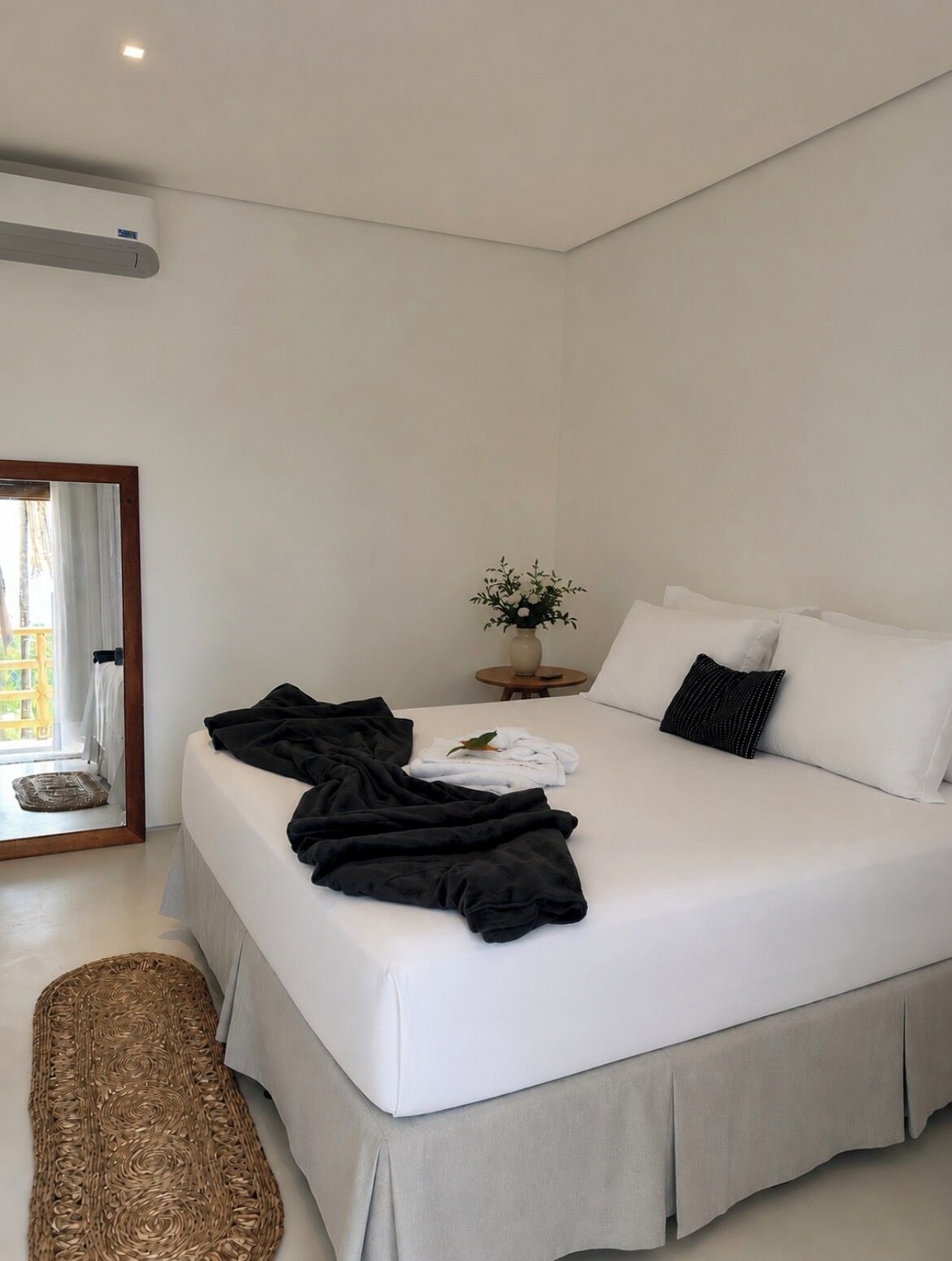 A modern hotel room with a large bed, a small round table with a plant, and a view of the outside through a door.