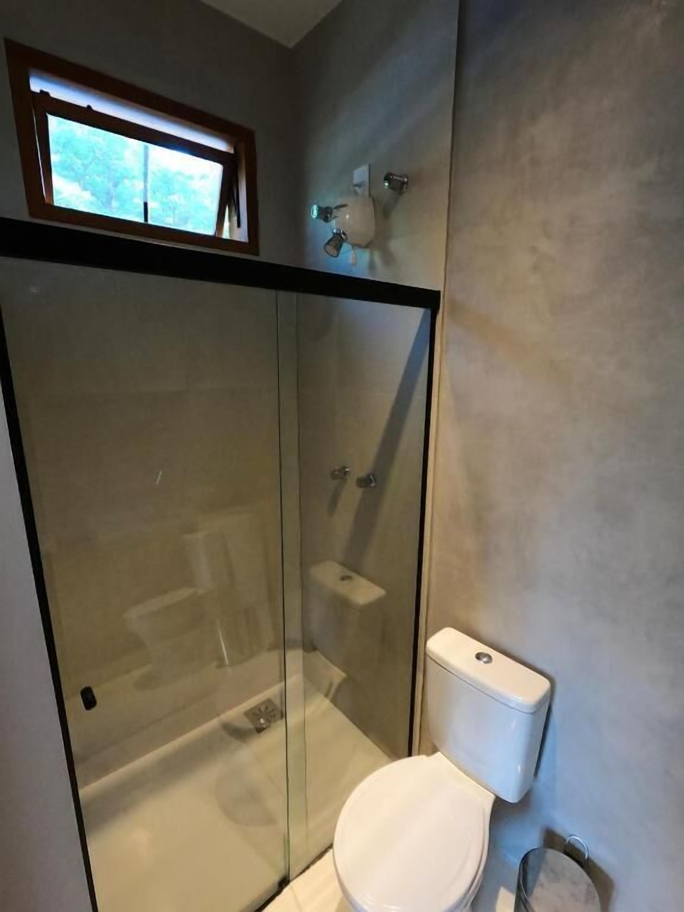 Un baño moderno con cabina de ducha de vidrio, inodoro y lavamanos pequeño.
