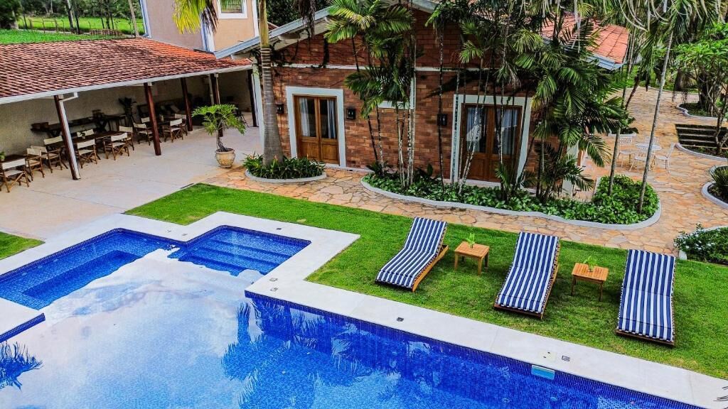 Un área de piscina con dos piscinas separadas, sillas de descanso y un porche cubierto con mesas y sillas.