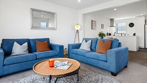 A modern living room with two blue sofas, a wooden coffee table, and a large mirror on the wall. - Central Christchurch 2 Bedroom Apartment – Balcony & Parking (Christchurch)