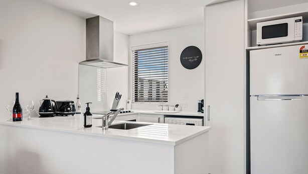 A modern kitchen with white cabinetry, a built-in microwave, and a stainless steel refrigerator. - Central Christchurch 2 Bedroom Apartment – Balcony & Parking (Christchurch)