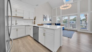 Une cuisine moderne avec des meubles blancs, un îlot central et une vue sur l’extérieur grâce à de grandes portes-fenêtres coulissantes.