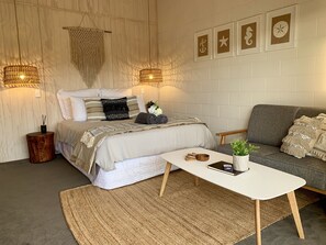 A bedroom with a bed, a grey sofa, a white coffee table, and a wall with nautical-themed decorations. - Kaikōura Peaks Studio Retreat 3 (Kaikoura)