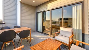 Une terrasse extérieure moderne, dotée d’une table et de chaises en bois, d’un canapé rembourré et d’une porte coulissante en verre donnant sur un balcon.