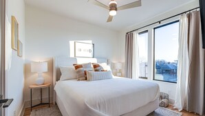 Une chambre dotée d’un grand lit, de deux tables de chevet avec des lampes, d’un ventilateur de plafond et offrant une vue sur l’extérieur grâce à de grandes fenêtres.