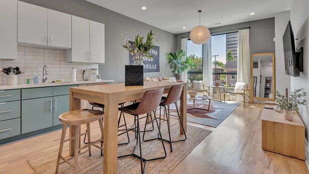 Une cuisine moderne avec un coin repas, comprenant une table en bois, des tabourets de bar et une grande fenêtre offrant une vue sur la ville.
