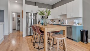 Une cuisine moderne avec des meubles blancs, un réfrigérateur en acier inoxydable, un îlot central en bois avec des tabourets et un vase agrémenté de plantes vertes.