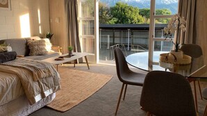 Quarto com cama, sofá, mesa de jantar e cadeiras, e vista para montanhas através de grandes janelas.