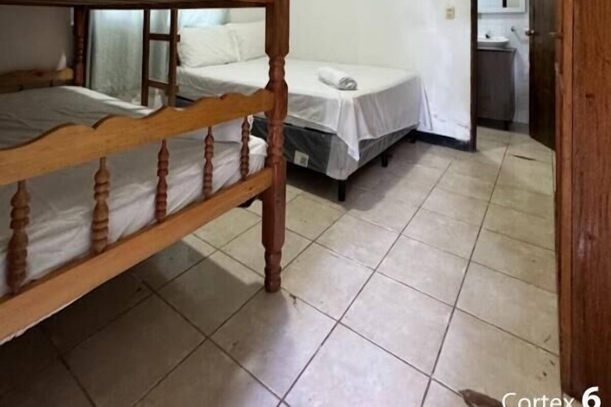 A room with a bunk bed, a single bed, and a bathroom with a sink and mirror.
