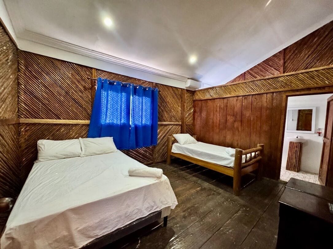 Una habitación con dos camas de madera, una cortina azul y un panel de pared de madera.