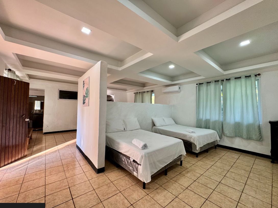 A room with two single beds, a wooden wardrobe, and a tiled floor.