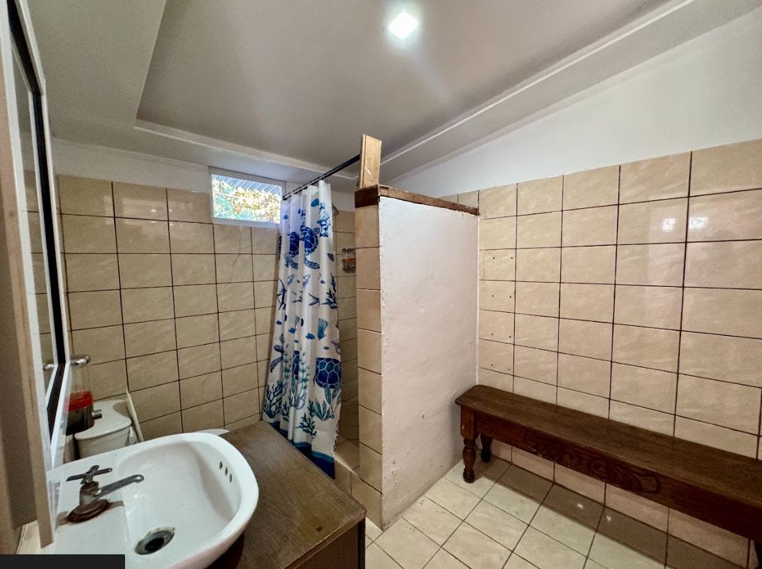 A bathroom with a sink, shower curtain, bench, and tiled walls.