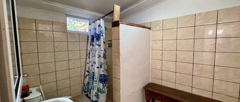 Un baño con lavamanos, cortina de ducha, banco y paredes de azulejos.