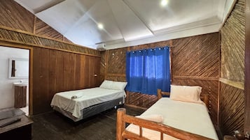 A room with two single beds, a wooden headboard, a small bedside table, and a window with blue curtains.