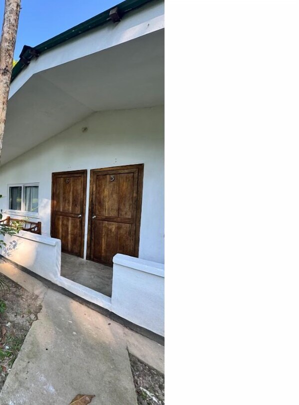Un edificio con fachada blanca, dos puertas de madera y un camino de hormigón que conduce a la entrada.