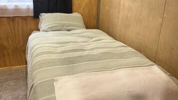 A neatly made bed with a striped bedspread and pillows, a framed picture on the wall, and a window with curtains.