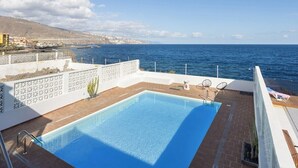 A rooftop pool with a clear view of the sea and a mountainous landscape in the background.