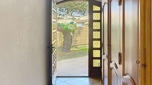 Un passadís amb sòl de rajola que condueix a una porta oberta amb vista a un jardí.