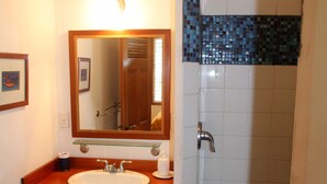 A bathroom with a wooden vanity, a white sink, a mirror, and a shower area with blue mosaic tiles. - Stay, relax and explore in Sunrise, our tropical oasis by the Caribbean Sea. (Punta Gorda)