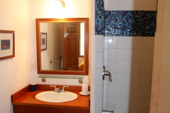 A bathroom with a wooden vanity, a white sink, a mirror, and a shower area with blue mosaic tiles. - Stay, relax and explore in Sunrise, our tropical oasis by the Caribbean Sea. (Punta Gorda)
