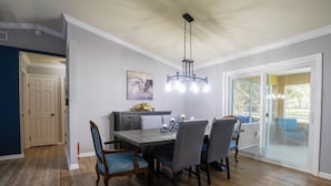 Un espace repas comprenant une table, des chaises, un lustre et une vue sur l’extérieur grâce à des portes vitrées.