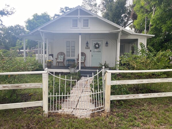A white building with a porch, two chairs, and a gate.