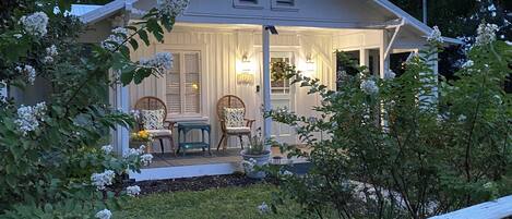 A house with a porch, two chairs, a table, and a potted plant.