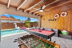 Zona de piscina con mesa de fútbol, sillas de descanso y un cartel que dice 'PLAY'.