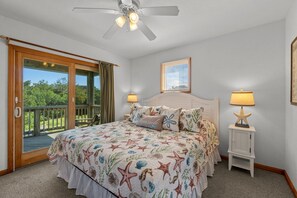 Un dormitorio con cama, dos lámparas de noche, ventilador de techo, ventana con persianas y vistas al exterior.