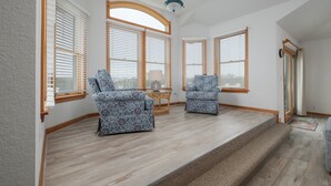 Une pièce spacieuse avec de grandes fenêtres, un escalier et deux fauteuils à motifs.