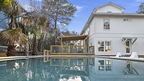 A swimming pool with a wooden deck and a white building in the background. - Crescent Oasis - Quiet Slice of 30A (Santa Rosa Beach)