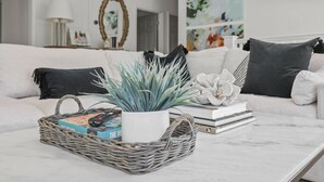 A living room with a white sofa, a wicker basket, a potted plant, and a remote control. - Crescent Oasis - Quiet Slice of 30A (Santa Rosa Beach)
