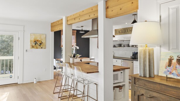 A modern kitchen with wooden beams, a dining area with clear chairs, and a kitchen counter with a coffee machine. - Crescent Oasis - Quiet Slice of 30A (Santa Rosa Beach)