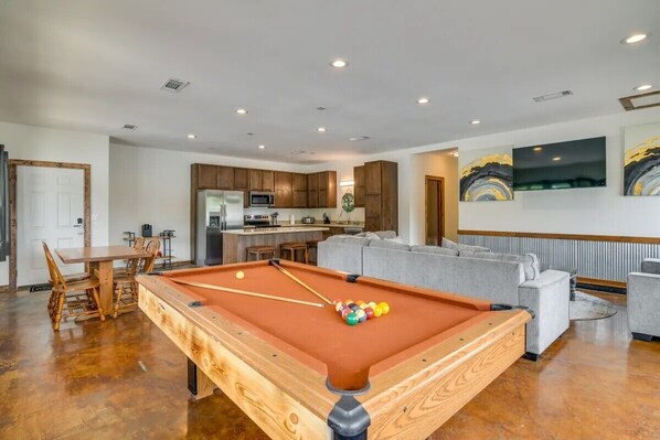 A spacious living area with a pool table, a dining table with chairs, a kitchen area, and a gray sofa. - Boats and Coves Unit 2 / Lots of Boat parking (Diamond City)