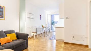 Un soggiorno moderno con un divano grigio, un'area pranzo con un tavolo in vetro e una cucina sullo sfondo.