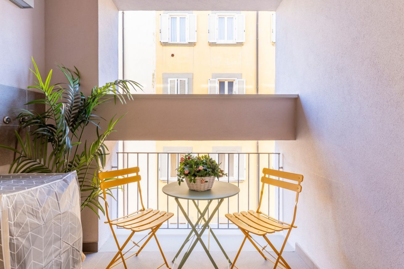 Un balcone con un tavolo e due sedie, una pianta in vaso, e un edificio sullo sfondo.