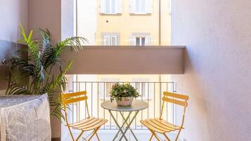 Un balcone con un tavolo e due sedie, una pianta in vaso, e un edificio sullo sfondo.