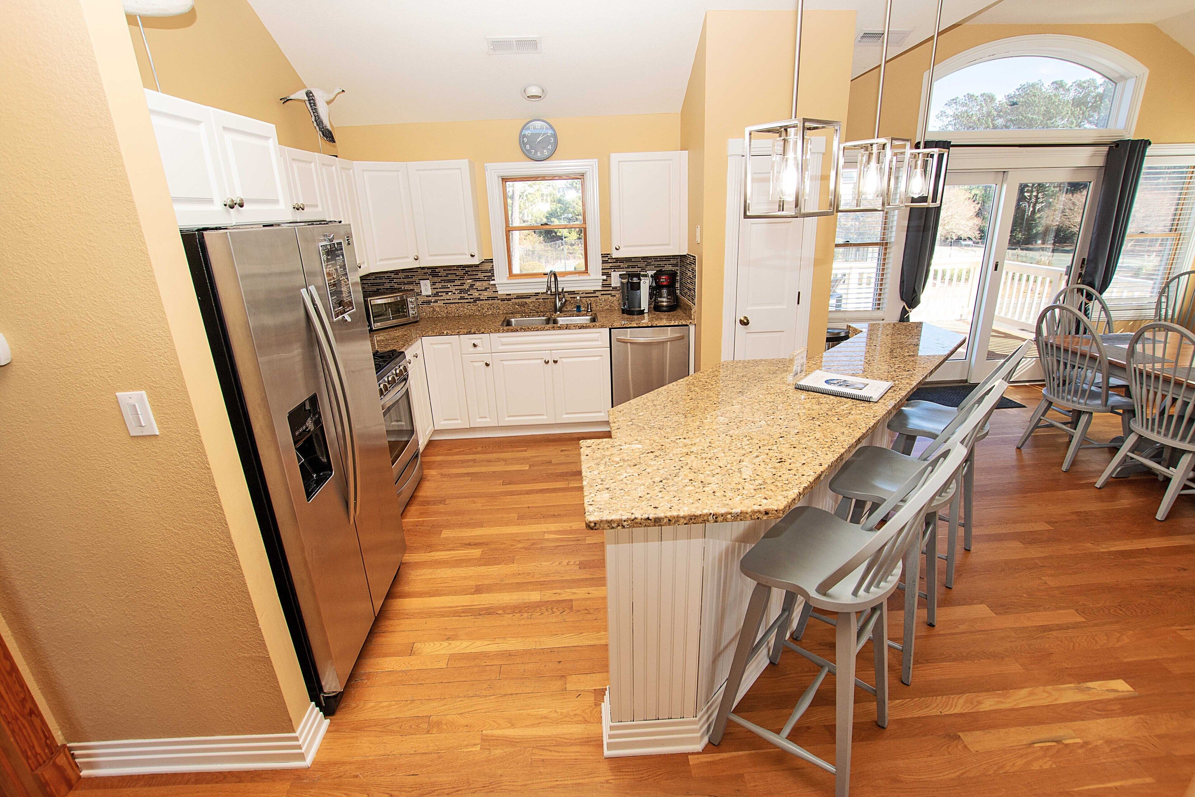 A kitchen with white cabinets, stainless steel appliances, a granite countertop, and a bar area with stools.