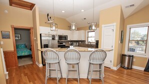 A kitchen with a central island, white cabinets, stainless steel appliances, and three bar stools.