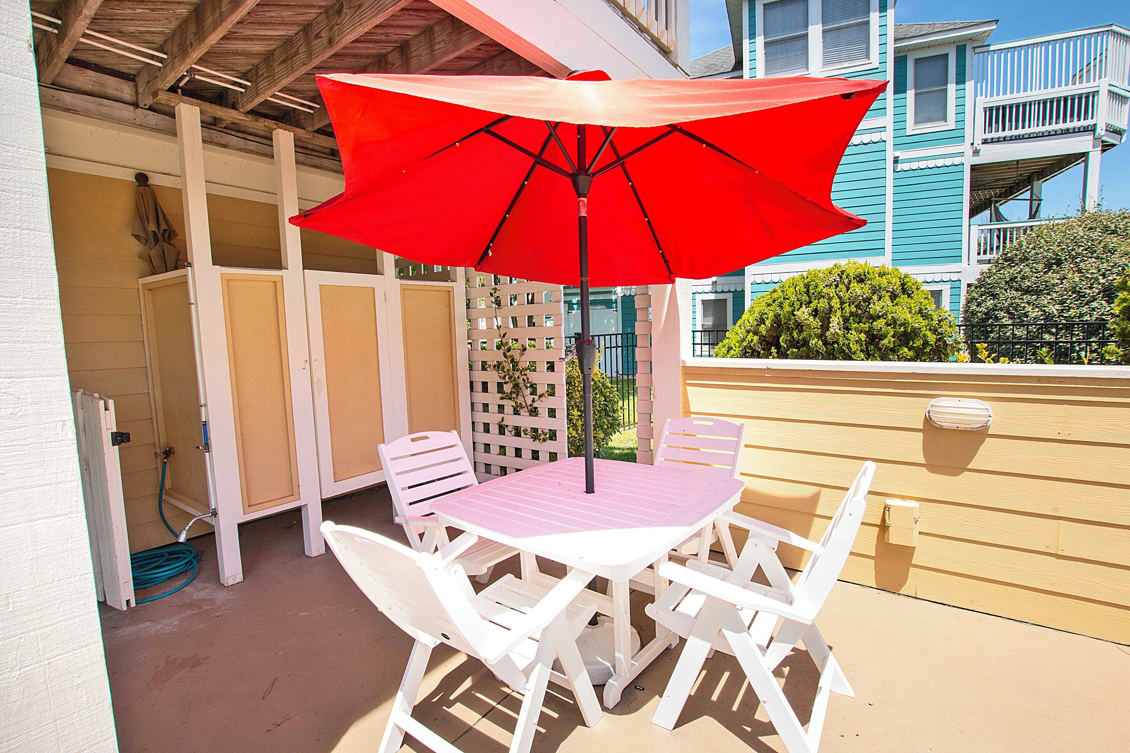 A patio with a white table and chairs, a red umbrella, and a wooden fence.