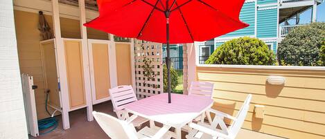 A patio with a white table and chairs, a red umbrella, and a wooden fence.