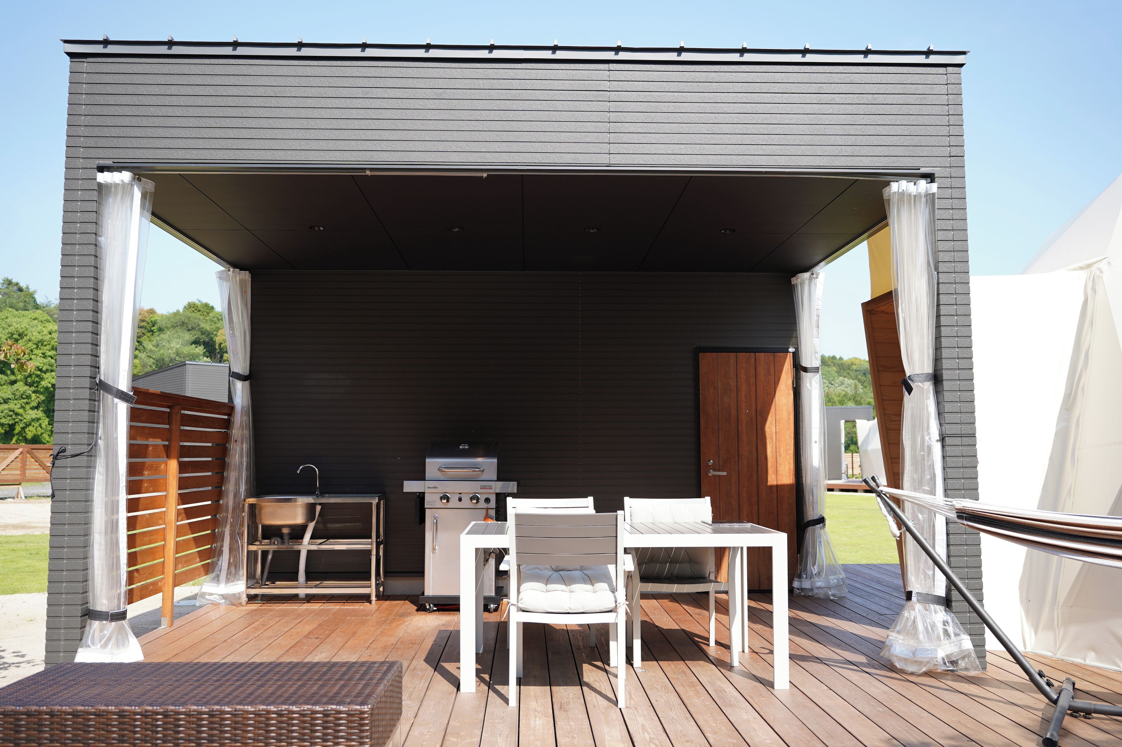 Un patio exterior con una parrilla, muebles blancos y un área techada.