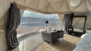 Amplia habitación con un ventanal que ofrece vistas a una zona boscosa. Hay un sofá, una mesita y una cama con ropa de cama blanca.