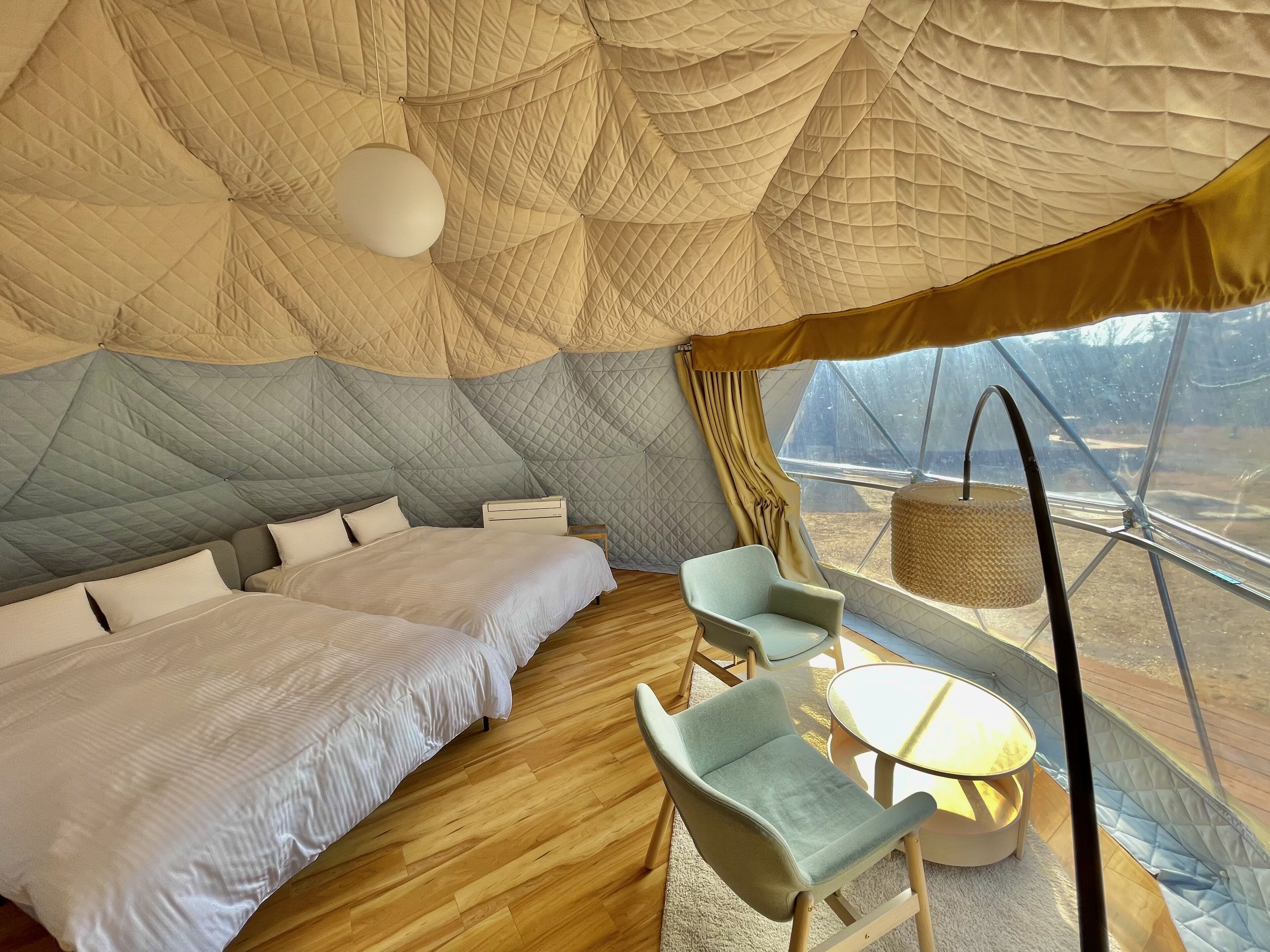 Ein gemütliches, helles Zimmer mit einem großen Bett, einem kleinen Tisch und Stühlen, mit einer einzigartigen, kuppelförmigen Decke und Blick ins Freie.