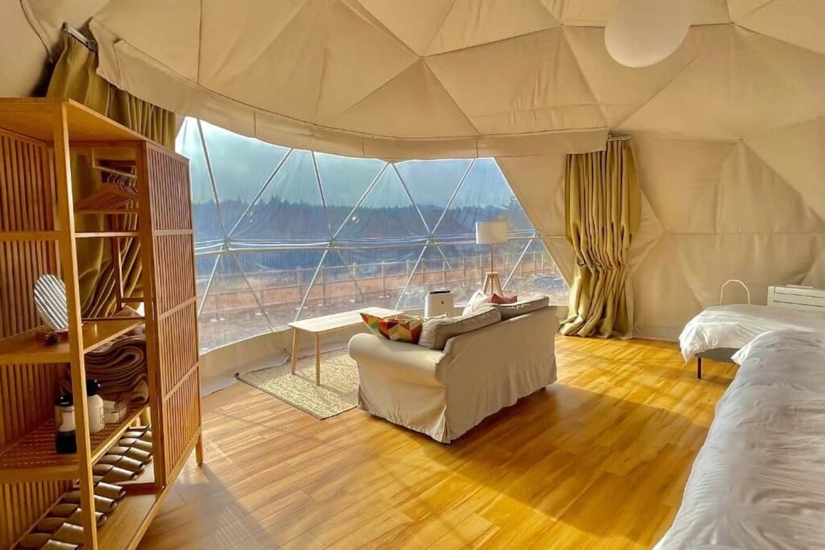 Um quarto espaçoso coberto por uma tenda, com piso de madeira, um sofá, uma cama e um guarda-roupa.