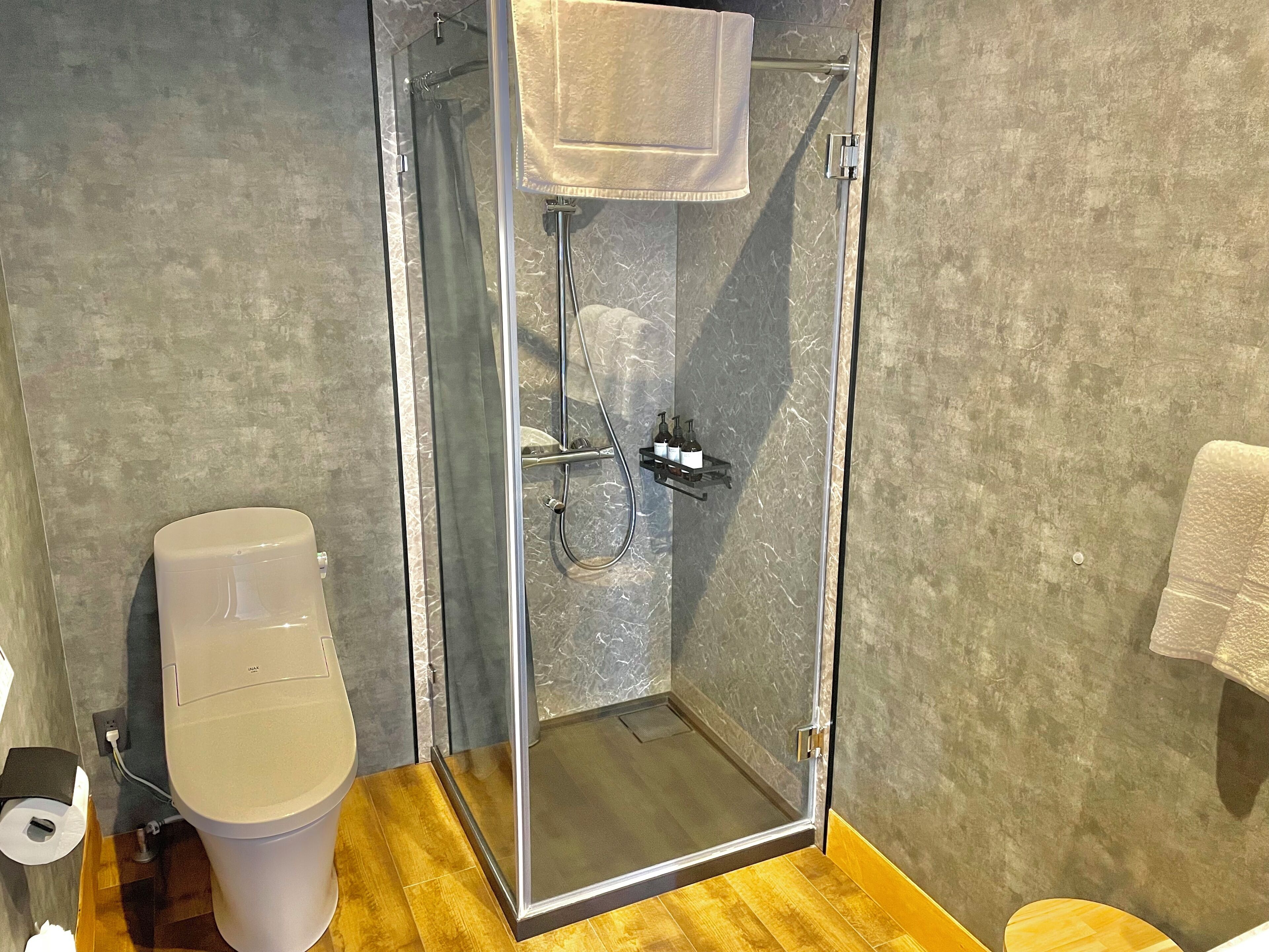 A modern bathroom with a glass-enclosed shower, a toilet, and a towel rack.