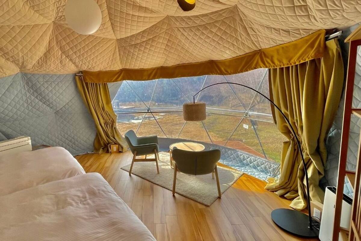 Quarto acolhedor com uma cama grande, uma mesa pequena com cadeiras e vista para o exterior através de uma janela.