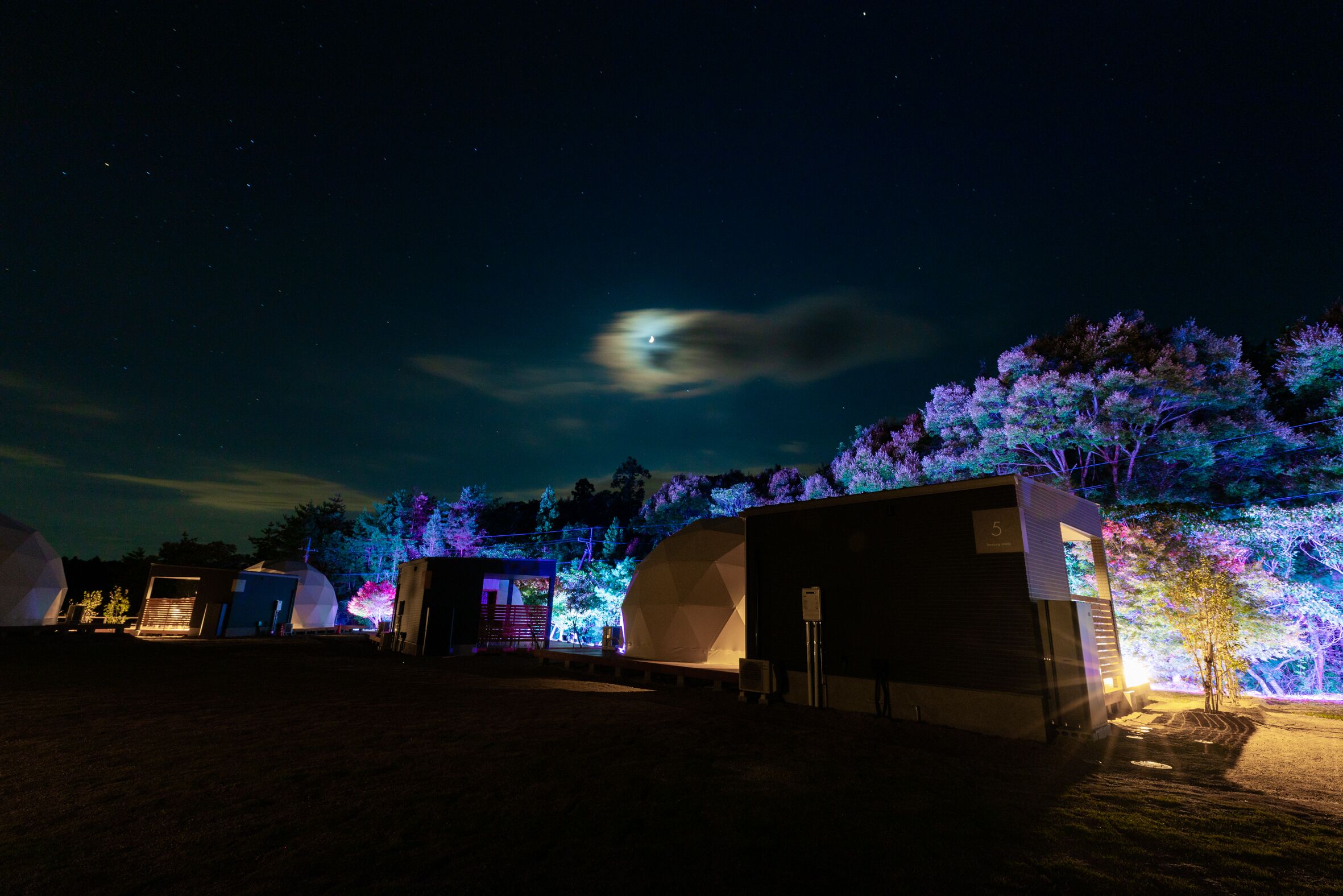A series of geodesic domes with a small building adjacent to them, under a night sky with visible stars and a moon.