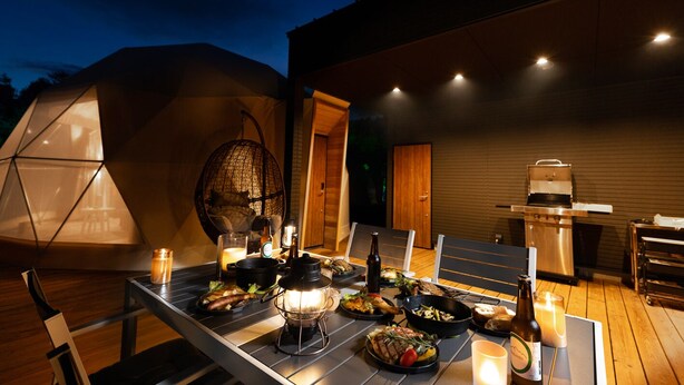Un espacio exterior para comer con una mesa preparada para una comida, un sillón colgante y una parrilla.