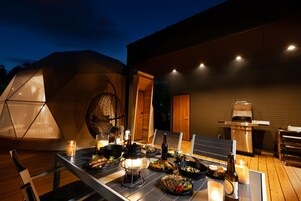 Un espacio exterior para comer con una mesa preparada para una comida, un sillón colgante y una parrilla.